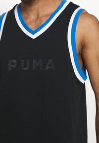 Man i svart ärmlös Puma sporttröja med blå och vit kant runt halsringningen och armhålorna.