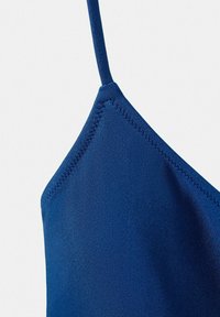 Close-up van een driehoek van marineblauwe stof met zigzagstiksels en een dunne band, waarschijnlijk onderdeel van een kledingstuk zoals een badpak of beha.