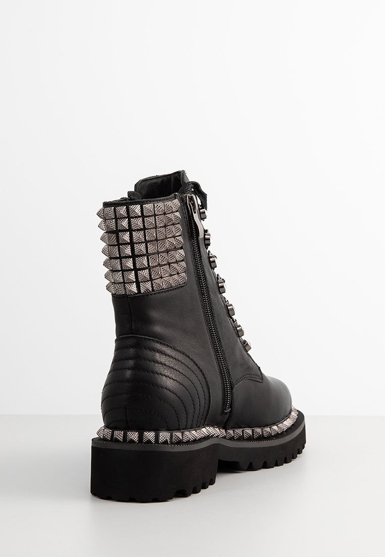 Stivale alla caviglia in pelle nera con retro testurizzato, dettagli con borchie, chiusura con zip e suola in gomma spessa. Presenta cuciture dettagliate.
