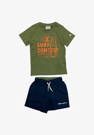 T-shirt verde a manica corta con scritta arancione "Surf Contest" e grafica di una tavola da surf, abbinata a pantaloncini blu navy con coulisse e logo bianco Champion.