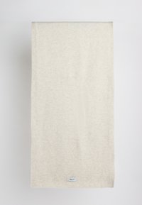 Couverture texturée couleur beige clair fabriquée en tissu doux, présentant un motif discret et une petite étiquette de marque cousue sur le bord inférieur.