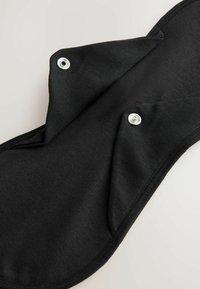 Czarna materiałowa podpaska menstruacyjna z zapięciami na napy, charakteryzująca się miękką teksturą i dwoma nakładającymi się klapami zapewniającymi pewne umiejscowienie.