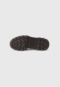 Black rubber shoe sole with textured grip pattern, featuring a prominent logo detail and rounded edges for stability.