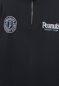 Pull-over noir avec col zippé. Présente le texte brodé blanc "Peanuts Hockey Club" et un logo circulaire avec la lettre "P".