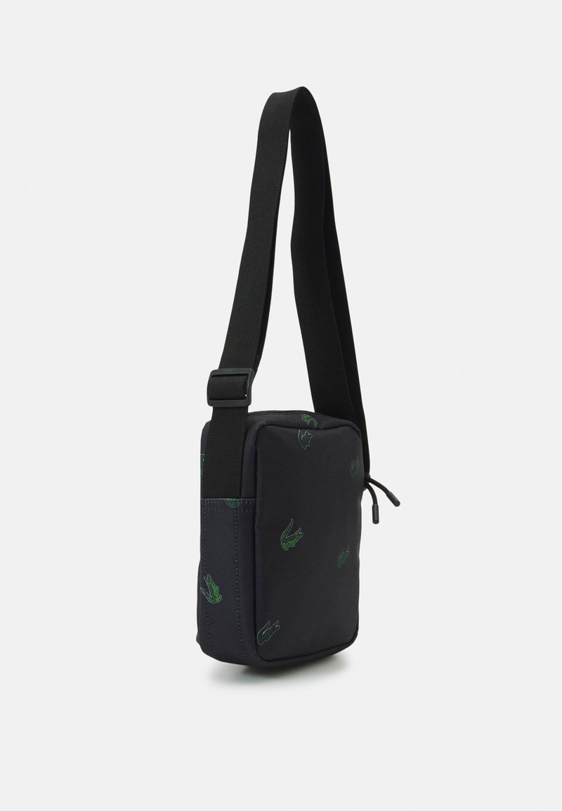 Sac à épaule en tissu noir avec des logos brodés verts, forme rectangulaire, bandoulière réglable et détail de fermeture à cordon.