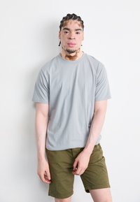 T-shirt en coton gris à manches courtes associé à un short vert olive. Le t-shirt possède un col rond et une coupe décontractée.