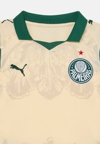 Maglia da calcio beige con colletto verde, caratterizzata da un logo Puma, badge del Palmeiras, stella rossa e un intricata trama chiara sulla stoffa.
