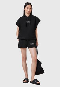 Svart bomullsblandad hoodie med oversized design, korta ärmar, snörning, sidoknappar, kombinerad med svarta shorts och plana slidesandaler.