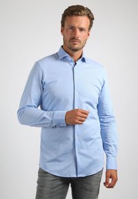 Lichtblauwe blouse met lange mouwen van gladde stof, met een klassieke kraag en knoopsluiting aan de voorkant, afgeronde onderkant en knoopmanchetten.
