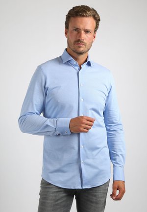 Lichtblauwe blouse met lange mouwen van gladde stof, met een klassieke kraag en knoopsluiting aan de voorkant, afgeronde onderkant en knoopmanchetten.