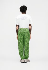 Fehér póló kék grafikával a hátulján, zöld nadrággal párosítva, amely pettyes mintázattal és húzózsinóros derékkal rendelkezik.