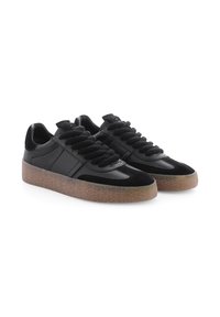 Ein Paar schwarze Ledersneaker mit dicken schwarzen Schnürsenkeln und durchsichtigen braunen Gummisohlen, schräg von der Seite auf weißem Hintergrund.