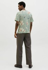 Šviesiai žalia gėlėta marškinėliai trumpomis rankovėmis ir laisvu siluetu, derinami su tamsiai pilkais plačiais kelnais ir juodais batais.