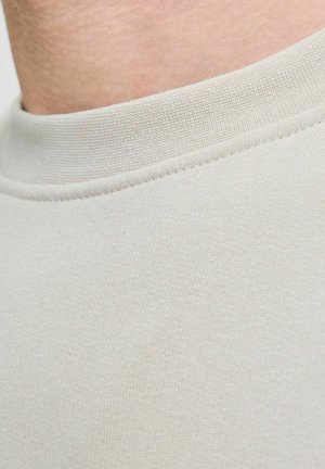 Tejido gris claro que muestra un primer plano de un cuello de tripulación con una textura suave y lisa, y un sutil detalle acanalado a lo largo del collar.