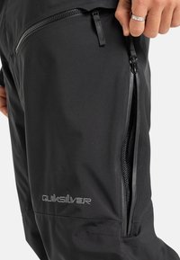 Zwarte waterdichte broek met een gladde textuur, voorzien van een zijzak met rits, Quiksilver-logo en een verstelbare taille.