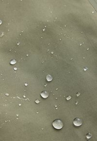 Des gouttelettes d'eau perlent sur une surface lisse en tissu imperméable vert olive.