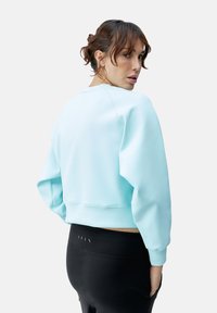 Lichtblauwe cropped sweatshirt met een ronde hals, geribde manchetten en een gladde textuur, gecombineerd met zwarte high-waisted leggings.