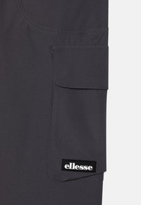 Grått tygfickor med sömmar och svart ellesse-logotyppatch. Slät textur med en praktisk fyrkantig form.