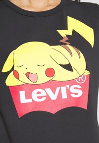 Svart t-shirt med en färgglad grafik av en sovande Pikachu på en röd Levi's-logga. Mjuk bomull, kort ärm, rund halsringning.