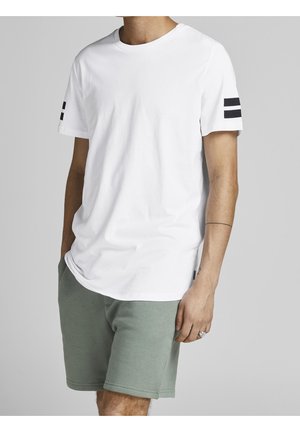 Weißes Baumwoll-T-Shirt mit Rundhalsausschnitt, kurzen Ärmeln und schwarzen Streifenakzenten am linken Ärmel; kombiniert mit grünen Shorts.