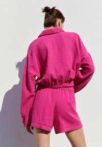 Shorts roses texturés et chemise oversize assortie à col. Le tissu semble léger et respirant avec une ceinture élastique.