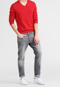 Suéter rojo de cuello en V, jeans grises y zapatillas blancas. Material de algodón con puños y dobladillo acanalados. Los jeans tienen un corte relajado y dobladillos enrollados.
