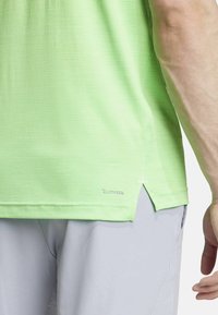 Groene textuur atletische shirt met zijsplitten en een "CLIMACOOL" logo op de zoom. Heeft een lichtgewicht, ademend ontwerp.