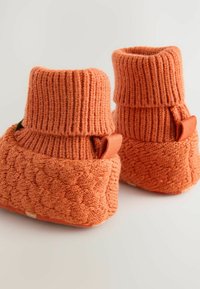 Bottillons tricotés orange avec une cheville côtelée, un corps texturé et de petites boucles en tissu de chaque côté. Matière douce et design chunky.