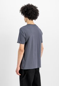 Graues Baumwoll-T-Shirt mit kurzen Ärmeln und rundem Halsausschnitt, mit lässigem Schnitt und minimalen Nähten. Rückansicht vor einem weißen Hintergrund.