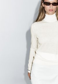 Roomkleurige coltrui gemaakt van zacht materiaal, gecombineerd met een glanzende witte rok. Eenvoudig ontwerp met lange mouwen en minimalistische details.