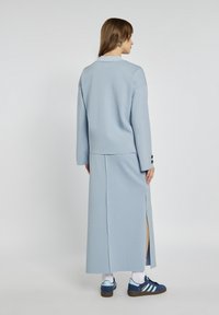 Jasnoniebieski dwuczęściowy strój składający się z krótkiego topu i długiej spódnicy z bocznymi rozcięciami, wykonany z miękkiego materiału, dopełniony ciemnoniebieskimi trampkami.