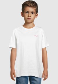 Camiseta de algodón blanca con mangas cortas, que presenta un pequeño gráfico de un corazón rosa en la parte izquierda del pecho. Cuello redondo y corte holgado.