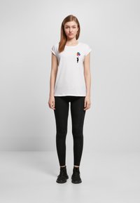 White cotton t-shirt with short sleeves and a round neckline, featuring a colorful balloon design on the left chest; paired with black leggings.