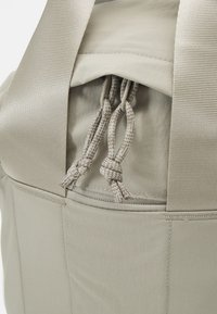 Gros plan d’un sac beige avec des bretelles en tissu et des cordons noués sur une poche ou une zone de fermeture.