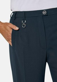 Marineblauwe broek van gladde stof, met een zijzak, riemlussen en een metallic hardware detail bij de taille.