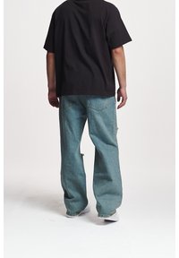 Černé bavlněné tričko s krátkými rukávy a volným střihem, doplněné světle modrými širokými džíny s kapsami na zadní straně a opotřebovanými detaily.