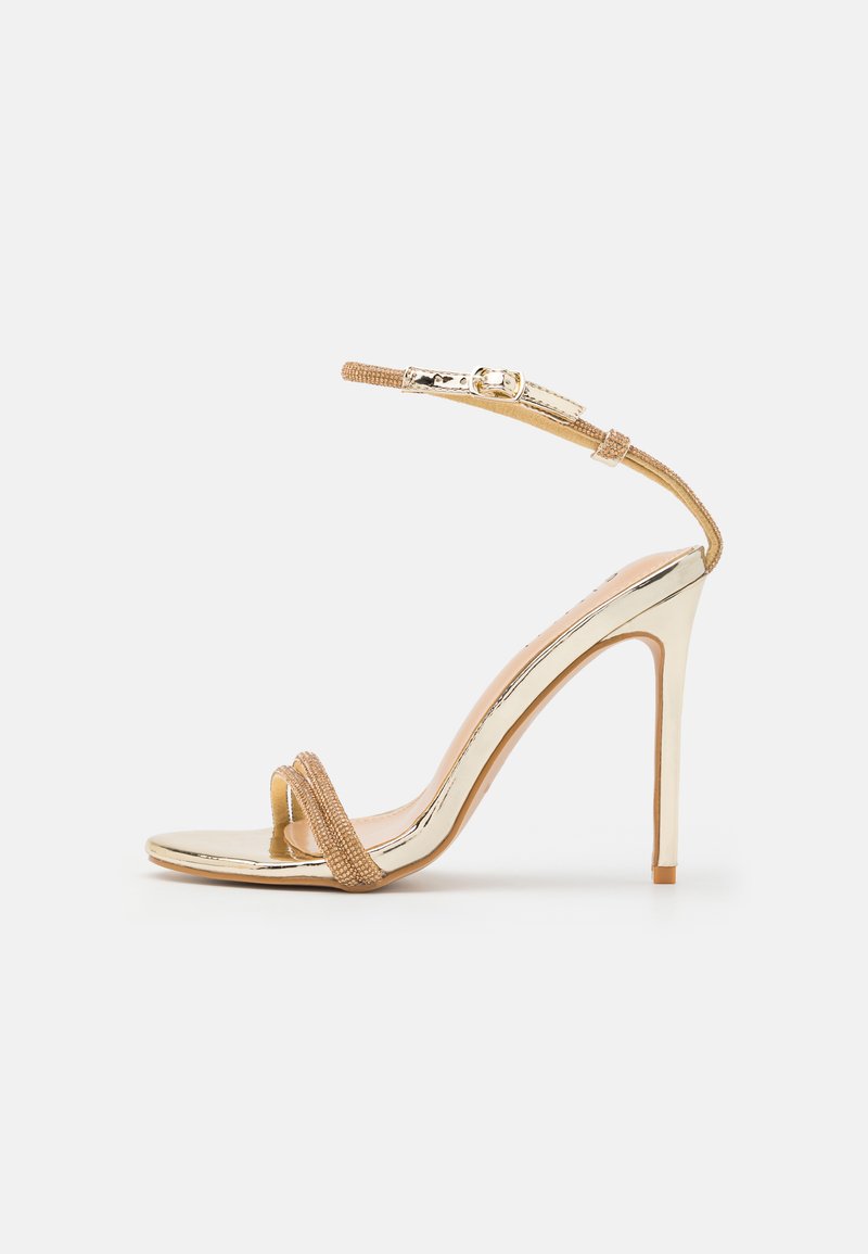 Sandal con tacco alto dorato, finitura metallica lucida, cinturino nude testurizzato e sottile cinturino alla caviglia fissato da una fibbia. Design open toe.