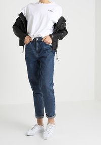 Black leather jacket, white short-sleeve T-shirt with text, blue high-waisted jeans, rolled cuffs, and white sneakers. Simple design.