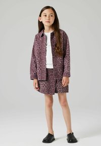 Lila blazer z leopardjim vzorcem s usklajenimi kratkimi hlačami, preložen preko bele majice. Črne slip-on čevlje dopolnjujejo outfit.