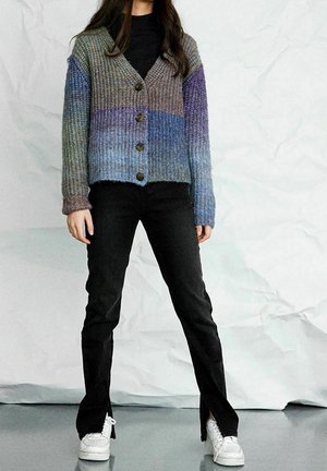 Sweter na drutach z gradientowym wzorem w odcieniach niebieskiego i szarości, z dekoltem w serek, długimi rękawami oraz pięcioma zapięciami na guziki. W połączeniu z czarnymi spodniami.