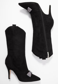 Bottines de cow-boy en suède noir à talons hauts, avec des orteils pointus, des accents décoratifs et une fermeture éclair sur le côté avec une languette de tirage. Surface texturée sur l'ensemble.