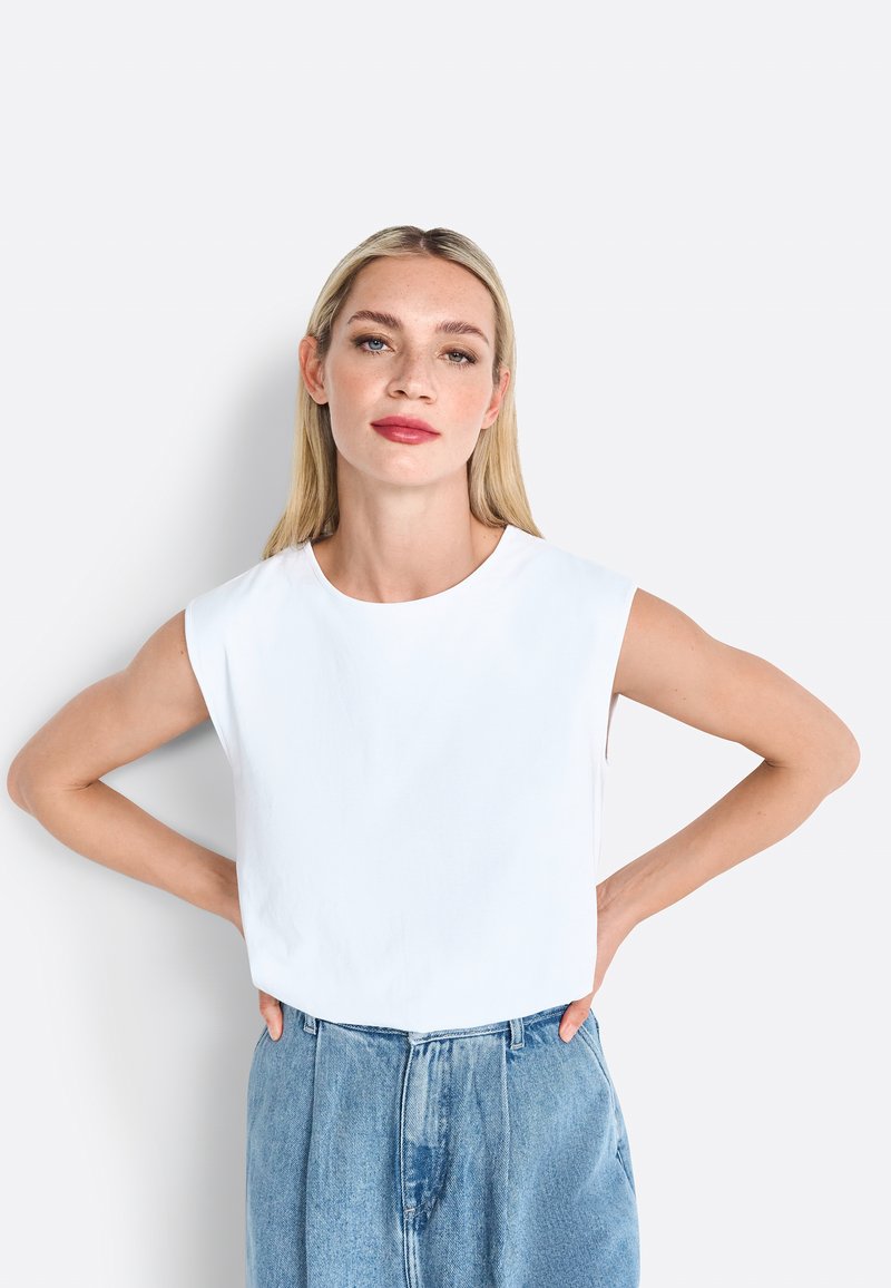 Hvid ærmeløs top med en rundudskæring, lavet af et glat, let stof. Kombineret med høj talje denimbukser i blå.