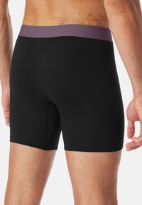 Schwarze Boxershorts mit lila Bund, aus weichem, dehnbarem Stoff gefertigt. Verfügt über ein enges Design und glatte Textur.