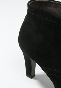 Botín de ante negro con tacón afinado, diseño curvado y costuras visibles. Forro interior suave y exterior texturizado.