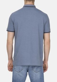 Herren Poloshirt mit kurzen Ärmeln in Hellblau, mit Kragen, besticktem marineblauen Saum an den Ärmeln und geradem Saum. Getragen mit Jeans.