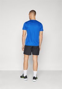 Camiseta de manga corta azul royal con cuello redondo, combinada con pantalones cortos negros. Lleva zapatos negros y calcetines blancos. Diseño simple y atlético.