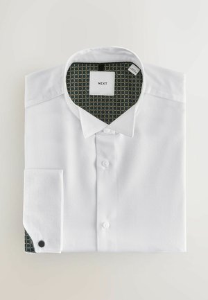 Hvid skjorte med knapper og tekstureret stof, foldet pænt. Indersiden af kraven har et grønt mønster med guldcirkler. Mærkeetiketten er synlig.