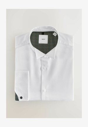 Hvid skjorte med knapper og tekstureret stof, foldet pænt. Indersiden af kraven har et grønt mønster med guldcirkler. Mærkeetiketten er synlig.