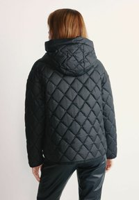Czarna pikowana kurtka puchowa z kapturem, z charakterystycznym wzorem w romby i gładką teksturą. Dół i mankiety wykończone są subtelnym wykończeniem.
