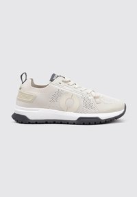 Zapatilla deportiva de color beige claro con parte superior de malla, logo circular y una media suela blanca. Suela exterior de goma negra con un patrón de agarre texturizado.